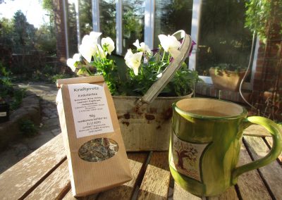 Teetasse und Teepackung vor einem Frühlingsgesteck im Garten